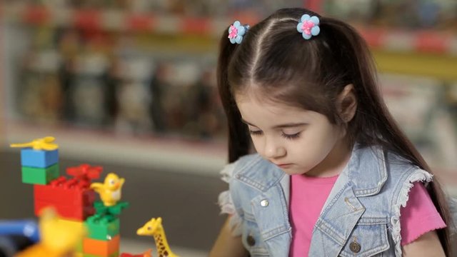 Cute little girl is playing with objects made of plastic elements, blocks of children's designers
