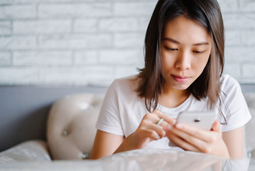 Relaxed asian woman use smart phone reading text message on white sofa.