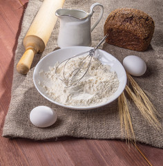 Ingredients for bakery products - milk, eggs, flour and rolling pin - on a rustic wooden background.