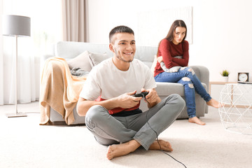 Angry woman looking at man who is playing video game at home