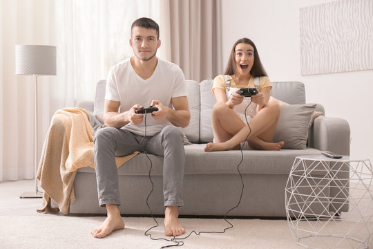 Emotional couple sitting on sofa and playing video game at home