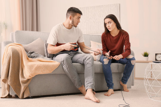 Angry woman cutting wire of controller while her boyfriend playing video game at home