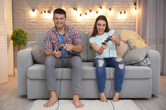 Emotional couple sitting on sofa and playing video game at home