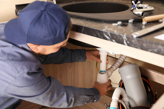 Professional male plumber replacing sink trap indoors