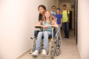 Fototapeta na wymiar Classmate helping girl in wheelchair at school corridor
