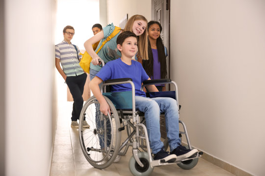 Girl Helping Boy In Wheelchair At School Corridor