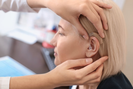 Otolaryngologist putting hearing aid in woman's ear in hospital