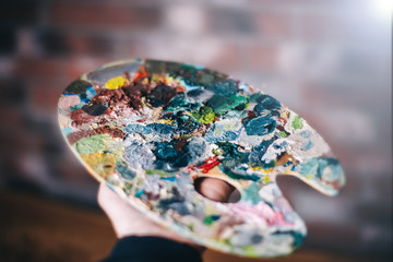 Palette with oil paints in the hands of the artist.