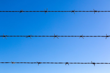 Close up view of barb wire fence against blue sky