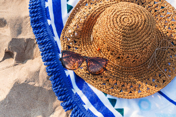 Women's straw hat decorated with beads and sunglasses on a beach towel on the beach, vacation, sand beach and sun. © Karina Kowalska