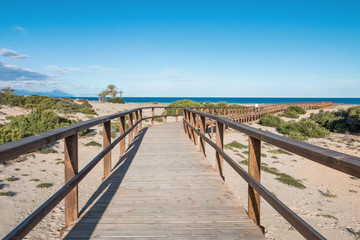 A wooden bridge leading to a sandy beach, in the distance the Mediterranean, sand and plants. Gran Alacant, Spain.