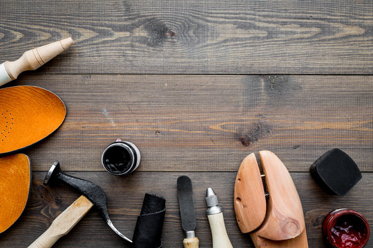 Work desk of shoemaker with instruments, wooden shoe and leather. Dark wooden background top view copy space