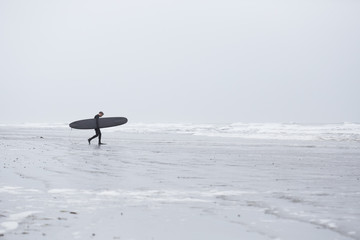 Man carrying surfboard and walking towards sea
