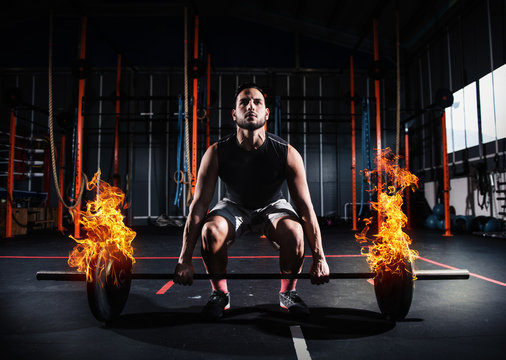 Athletic man works out at the gym with a fiery barbell