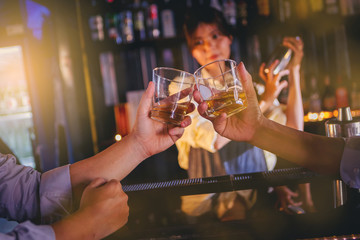 Drunk men crank the glass of alcohol at the bar in nightclub, female bartender as background. Selected focus