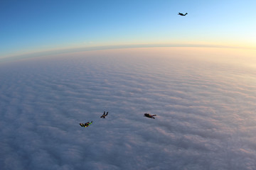 Skydivers are flying above pink clouds.