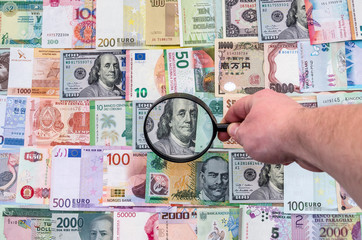 Male hand with magnifier checking world banknotes
