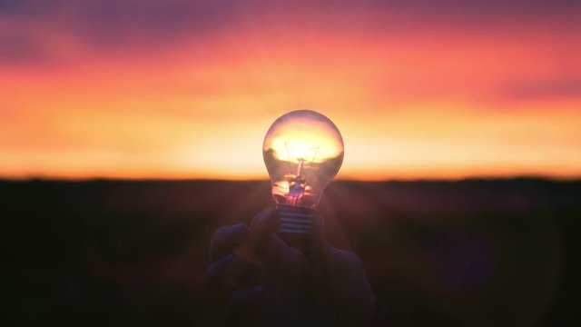 Silhouette of a hand holding lamb bulb on sunset