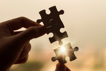 Silhouette Woman hands connecting couple puzzle piece against sunrise effect, businesswoman holding jigsaw with sunset background. Business solutions, target, success, goals and strategy concepts