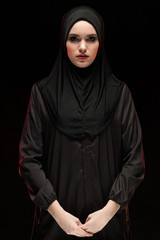 Portrait of woman in hijab standing against black background