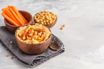 Hummus, fresh carrot sticks and boiled chickpeas in wooden bowls. Vegan food concept, light background, copy space, top view