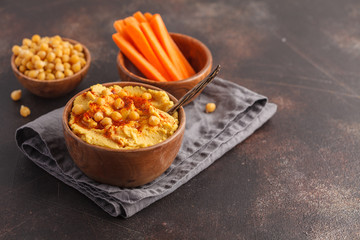 Hummus, fresh carrot sticks and boiled chickpeas in wooden bowls. Vegan food concept, dark background, copy space.