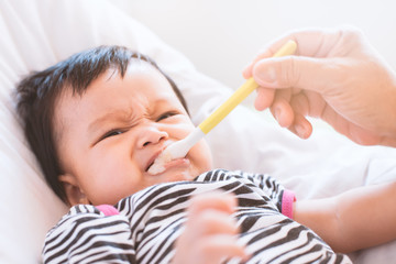 Mother feeding cute asian baby girl with a spoon at home. Little baby girl eating her meal with innocence.