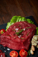 Composition of raw beefsteak on slate board with vegetables and seasoning, selective focus, close-up, vertical