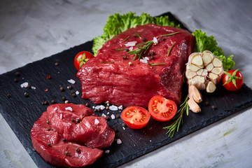 Composition of raw beefsteak on slate board with vegetables and seasoning, selective focus, close-up.