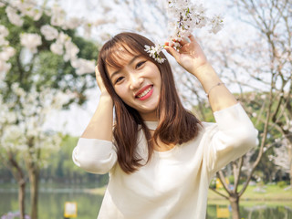 Outdoor portrait of beautiful young Chinese girl smiling among blossom cherry tree brunch in spring garden, beauty, summer, emotion, expression and people concept.