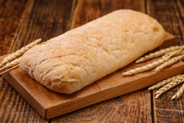 Fresh tasty homemade bread on a wooden board. A monotonous still life with bread and spikelets of rye.