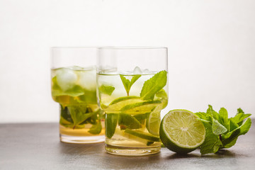 Brazilian traditional caipirinha with lime, sugar and mint in glasses. White background, dark table, copy space.