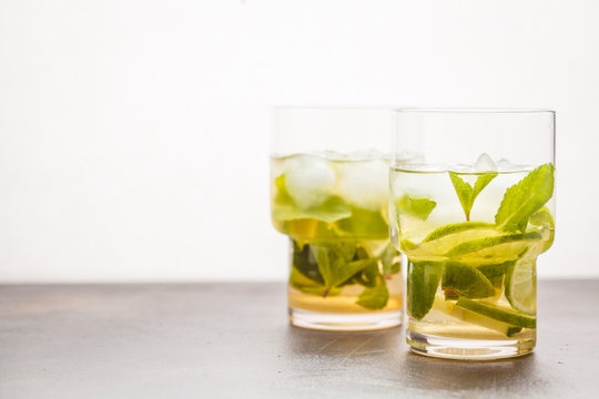 Brazilian traditional caipirinha with lime, sugar and mint in glasses. White background, dark table, copy space.