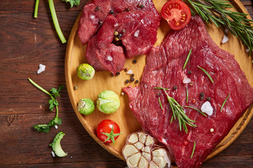Still life of raw beef meat with vegetables on wooden plate over vintage background, top view, selective focus