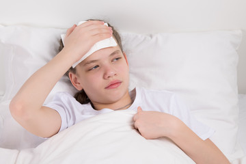 The girl on the bed, holds her hand on her forehead to relieve pain