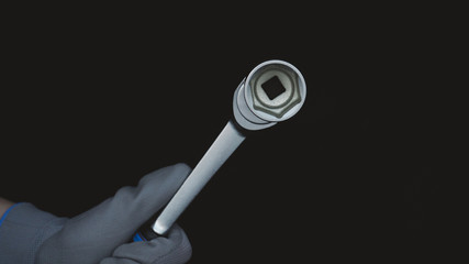 A builder or a repairman in gloves holds a wrench, a black background.