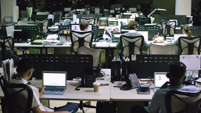 PAN of helpdesk operators in headsets sitting at their desks and talking with customers