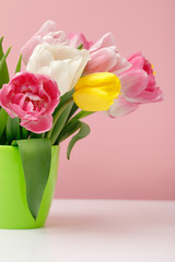 Green vase with spring tulips on pink background