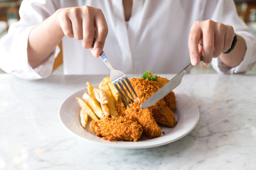 Closeup image of a hands using knife and fork to eating french fries and fried chicken in restaurant