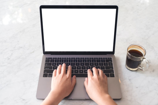 Top view mockup image of hands using and typing on laptop with blank white desktop screen and coffee cup on marble table in cafe