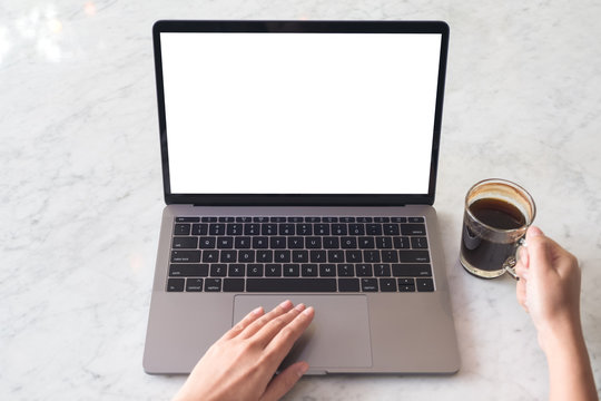 Top view mockup image of hands using laptop with blank white desktop screen while drinking coffee on marble table in cafe