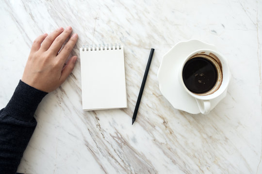 Top View Image Of A Hand Going To Write Down On A Blank White Notebook With Coffee Cup On Table