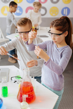 Chemistry lovers. Two pleasant classmates using pipettes and adding some chemicals to the test tubes while conducting an experiment during chemistry class