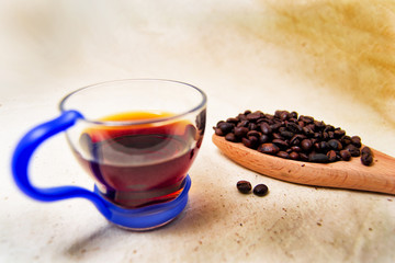 soft focus of a cup of energetic drink infusion and coffee beans on a wooden spoon with a raw background. for detox and healthy concept
