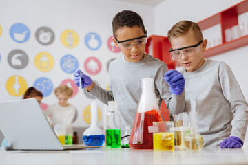Love experimenting. Two pleasant teenage friends adding chemicals into the flask with a pipette and observing the reaction during their chemistry class in the lab
