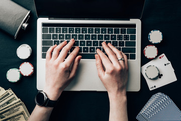 Woman hands on laptop by cards and chips on casino table