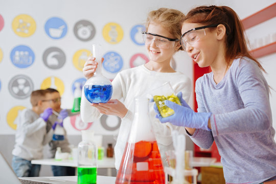 Right reaction. Two cheerful teenage schoolgirls holding flasks with chemical substances and checking them for the desired chemical reaction in them