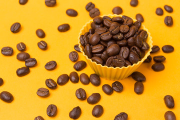 coffee beans in a yellow container on a yellow background, other grains scattered around