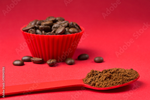 Red Spoon With Ground Coffee Powder In The Foreground And Beans A Container Red Spoon With Ground Coffee Powder In The Foreground And Beans A Container