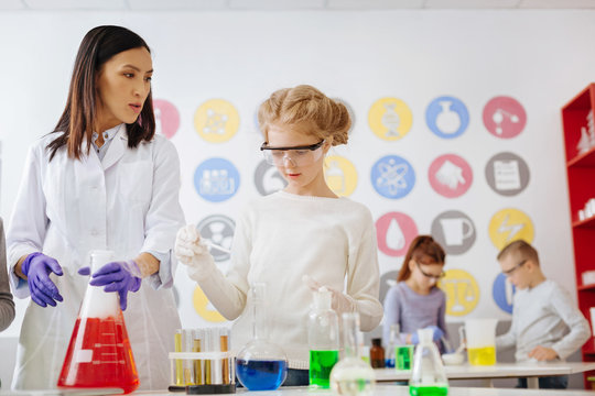 Best supervisor. Caring female teacher and her teenage student carrying out a chemical experiment together while the girl being about add some agent into the flask